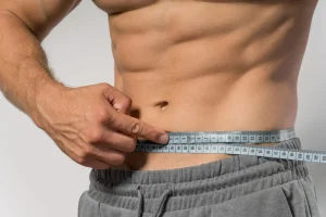 fit man holding measuring tape around waist with a contoured abdomen